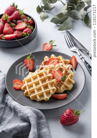Homemade soft waffles with fresh strawberries in a plate on a light background. Homemade soft waffles with fresh strawberries in a plate on a light background. 118173217