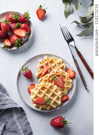 Homemade soft waffles with fresh strawberries in a plate on a light background. Homemade soft waffles with fresh strawberries in a plate on a light background. 118173219