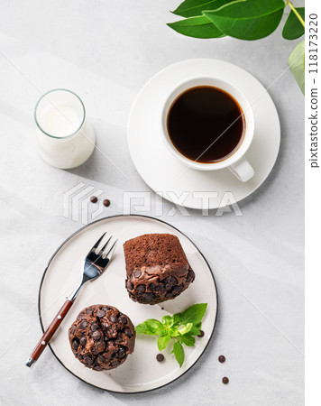 Chocolate muffins on a white plate with mint on a light background with cup of coffee, milk Chocolate muffins on a white plate with mint on a light background with cup of coffee, milk 118173220