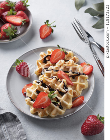Homemade soft waffles with fresh strawberries and chocolate topping in a plate on a light background Homemade soft waffles with fresh strawberries and chocolate topping in a plate on a light background 118173223