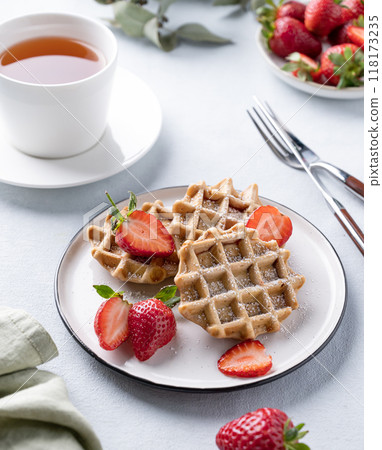 Homemade soft waffles with fresh strawberries and powdered sugar in a plate on a light background Homemade soft waffles with fresh strawberries and powdered sugar in a plate on a light background 118173235