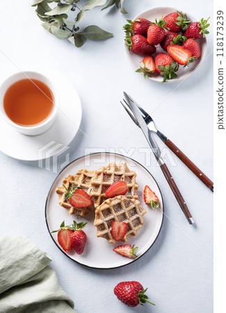 Homemade soft waffles with fresh strawberries and powdered sugar in a plate on a light background  118173239