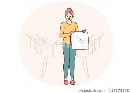 Woman housewife stands near dryer with clean towels doing household chores to create comfort 118173568