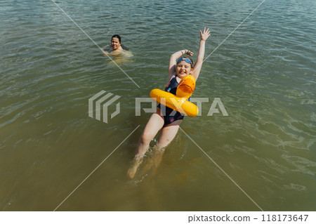 A girl is swimming with an inflatable yellow duck in the lake under her mother's supervision. She is enjoying a safe summer swim while her mother ensures her safety and care 118173647