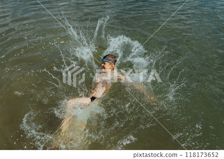 Boy splashing in the lake on a sunny summer day. Playful child having fun in the water with splashes all around. 118173652