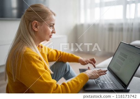 A blonde woman is working with intense focus from her home office, typing on a laptop A blonde woman is working with intense focus from her home office, typing on a laptop 118173742