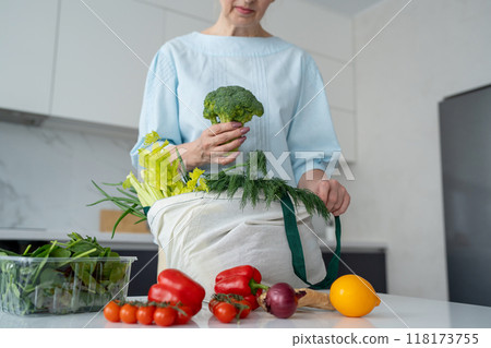 In a contemporary kitchen, a woman is unloading fresh groceries using ecofriendly bags 118173755