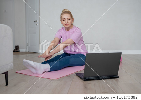 A woman is engaging in an online home exercise and stretching routine on a pink mat. Online fitness. 118173882