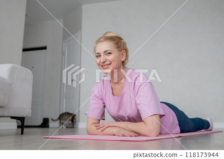 A woman is engaging in an online home exercise and stretching routine on a pink mat. Online fitness. 118173944
