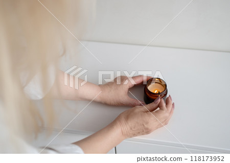 A woman is lighting a candle in her cozy home, near a reed diffuser, creating a calm atmosphere A woman is lighting a candle in her cozy home, near a reed diffuser, creating a calm atmosphere 118173952