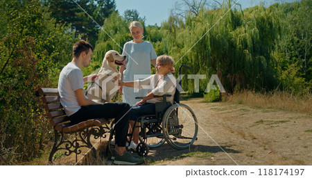 A family with a dog spending time outdoors, including a woman in a wheelchair and two other adults. A family with a dog spending time outdoors, including a woman in a wheelchair and two other adults. 118174197