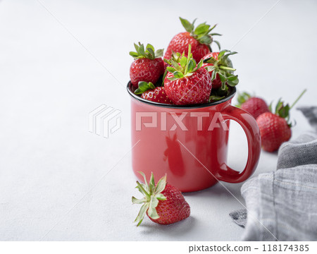 Juicy strawberries in a red cup on a light  background with napkin. Farm ripe healthy berries 118174385
