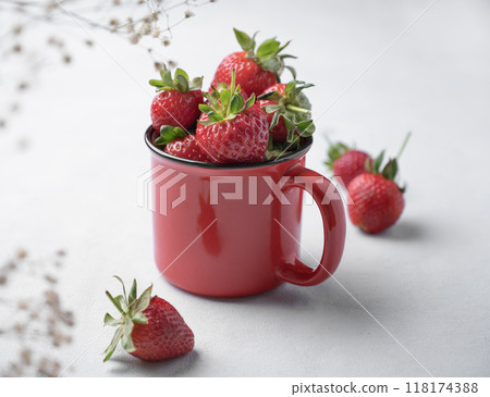 Juicy strawberries in a red cup on a light background with flowers. Farm ripe healthy berries. Juicy strawberries in a red cup on a light background with flowers. Farm ripe healthy berries. 118174388