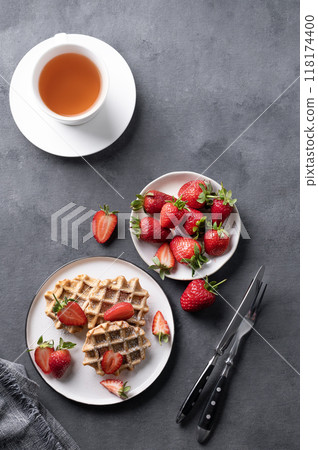 Homemade soft waffles with fresh strawberries and powdered sugar in a plate on a dark background Homemade soft waffles with fresh strawberries and powdered sugar in a plate on a dark background 118174400