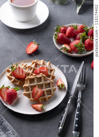 Homemade soft waffles with fresh strawberries and powdered sugar in a plate on a dark background  118174402