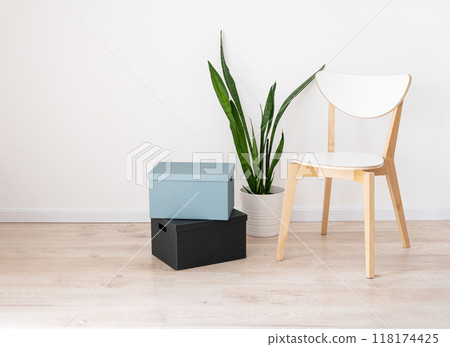 White wooden chair, cardboard boxes and a houseplant in a pot on a beige oak floor and gray wall White wooden chair, cardboard boxes and a houseplant in a pot on a beige oak floor and gray wall 118174425