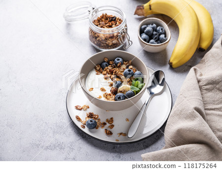 Muesli with vegetarian yogurt, banana and blueberries in a bowl on a gray texture background.  118175264