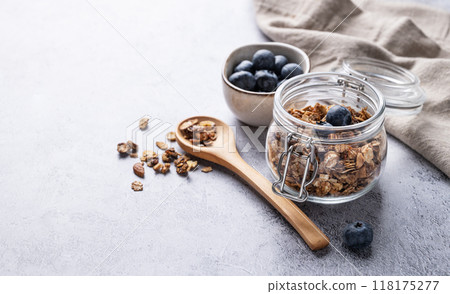 Homemade baked granola with nuts and fresh blueberry in a jar on a light background. 118175277