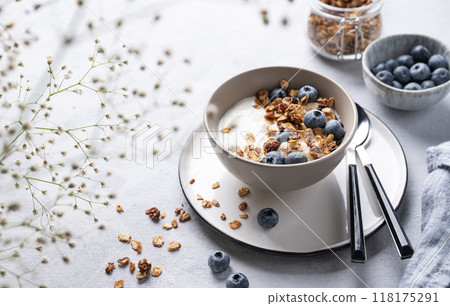 The concept of a healthy breakfast of yogurt, granola and fresh blueberry on a light background with flowers. Homemade diet and protein food. 118175291