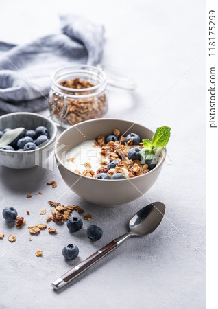 The concept of a healthy breakfast of yogurt, granola and fresh blueberry on a light background. The concept of a healthy breakfast of yogurt, granola and fresh blueberry on a light background. 118175299
