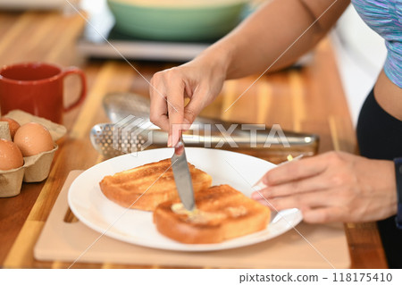 Close up shot of woman spreading butter on toasted bread with a cutlery knife Close up shot of woman spreading butter on toasted bread with a cutlery knife 118175410