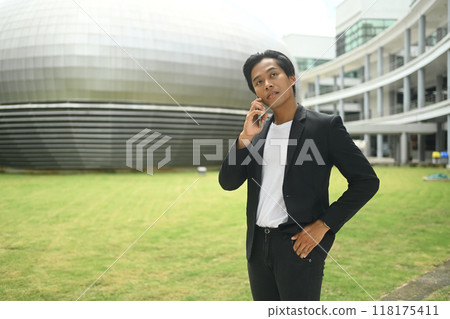 Young businessman talking on mobile phone standing outside modern office building Young businessman talking on mobile phone standing outside modern office building 118175411