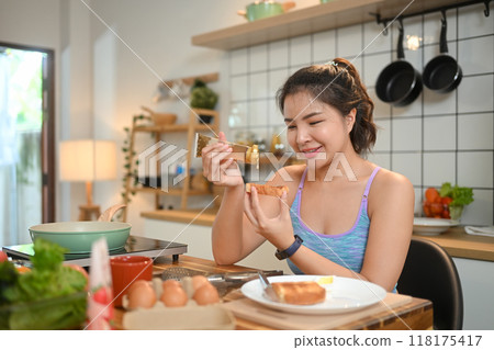 Smiling young woman pouring fresh honey on toast, enjoy healthy breakfast in the kitchen 118175417