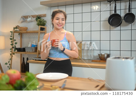 Happy young fitness woman enjoying cup of coffee at morning in her kitchen Happy young fitness woman enjoying cup of coffee at morning in her kitchen 118175430
