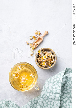 Chamomile herbal tea in a glass cup on a light background with dry flowers and napkin.  118175464