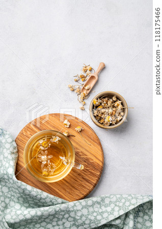 Chamomile herbal tea in a glass cup on a wooden board on a light background with dry flowers.  118175466