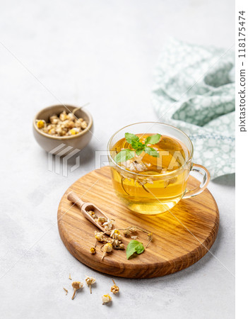 Chamomile herbal tea in a glass cup with mint on a light background with dry flowers. Chamomile herbal tea in a glass cup with mint on a light background with dry flowers. 118175474