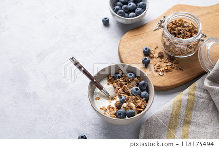 The concept of a healthy breakfast of yogurt, granola and fresh blueberry on a light background. The concept of a healthy breakfast of yogurt, granola and fresh blueberry on a light background. 118175494