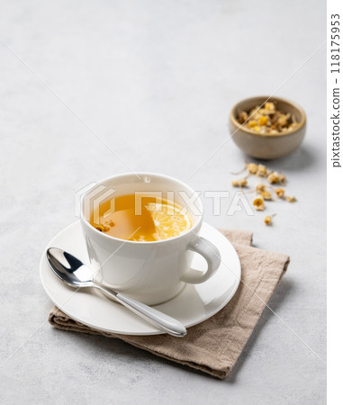 Chamomile herbal tea with lemon in a white cup on a light background with dry flowers. Chamomile herbal tea with lemon in a white cup on a light background with dry flowers. 118175953