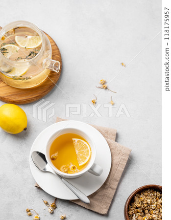Chamomile herbal tea with lemon in a white cup and teapot with flowers on a light background.  118175957