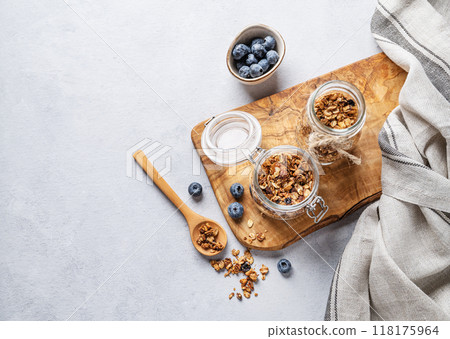 Homemade baked granola with nuts and fresh blueberry in a jar on a light background. 118175964
