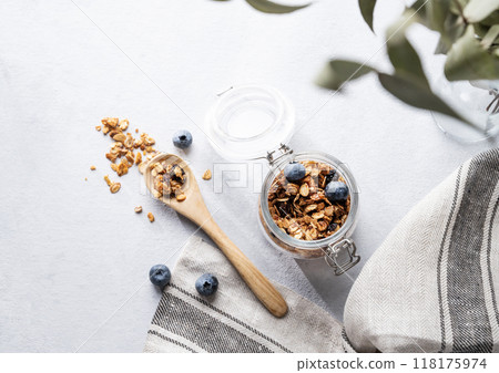 Homemade baked granola with nuts and fresh blueberry in a jar on a light background with napkin  118175974
