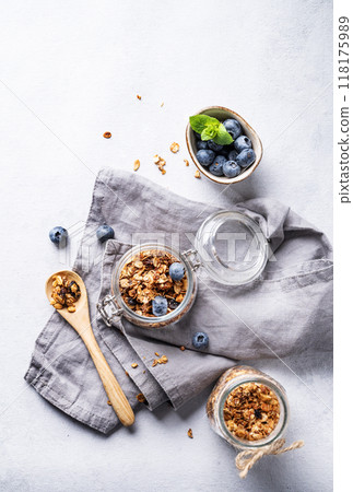 Homemade baked granola with nuts and fresh blueberry in a jar on a light background with napkin. Homemade baked granola with nuts and fresh blueberry in a jar on a light background with napkin. 118175989