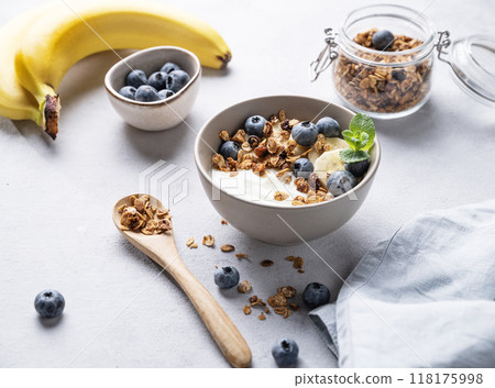 Homemade baked granola with yogurt, blueberries and banana in a bowl on a light background Homemade baked granola with yogurt, blueberries and banana in a bowl on a light background 118175998