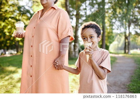 African American boy biting ice cream while holding grannys hand, they spending pastime in verdant park 118176863