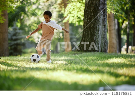 Little African American boy improving football skill during warm summer day in park Little African American boy improving football skill during warm summer day in park 118176881