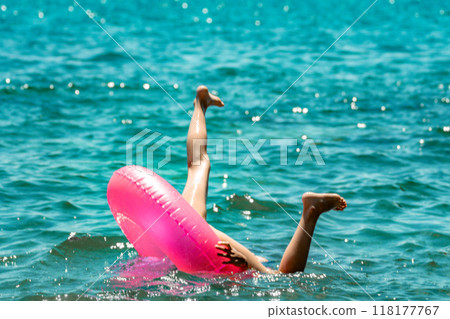 Legs, Pink Float, Ocean Water: A person falls out of a pink inflatable ring in the ocean. Legs, Pink Float, Ocean Water: A person falls out of a pink inflatable ring in the ocean. 118177767