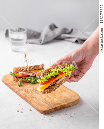 Hands holding a club sandwich with bacon, cheese, tomato and lettuce on a wooden board  118177821