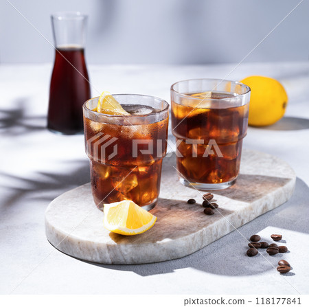 Cold brew coffee in a two glasses with lemon and ice on a marble board on a light background Cold brew coffee in a two glasses with lemon and ice on a marble board on a light background 118177841