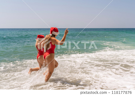 Women in Santa Claus hats run into the sea dressed in red swimsuits. Celebrating the New Year in a hot country Women in Santa Claus hats run into the sea dressed in red swimsuits. Celebrating the New Year in a hot country 118177876