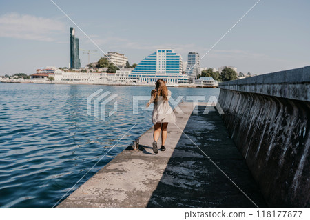 woman in a white dress is walking on a pier near the water. The scene is peaceful and serene, with the woman's long hair blowing in the wind. woman in a white dress is walking on a pier near the water. The scene is peaceful and serene, with the woman's long hair blowing in the wind. 118177877