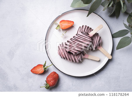 Chocolate cake pops ice cream on a stick in pink glaze on a plate with berries and eucaluptus  118178264