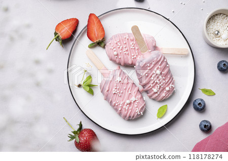 Cake pops ice cream on a stick in pink glaze on a plate with berries on a light background. Cake pops ice cream on a stick in pink glaze on a plate with berries on a light background. 118178274