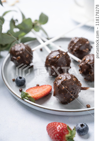 Chocolate cake pops with nuts on a plate with fresh berries on a light background close up.  118178278