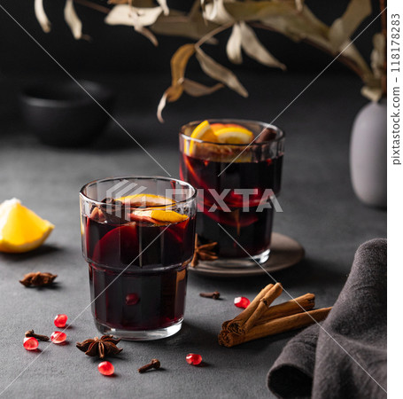 Mulled wine with orange, apple, pomegranate and cinnamon in glasses on a dark background. Mulled wine with orange, apple, pomegranate and cinnamon in glasses on a dark background. 118178283