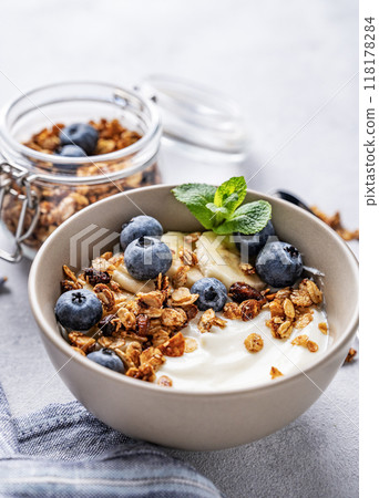 Muesli with vegetarian yogurt, banana and blueberries in a bowl on a light background close up.  118178284